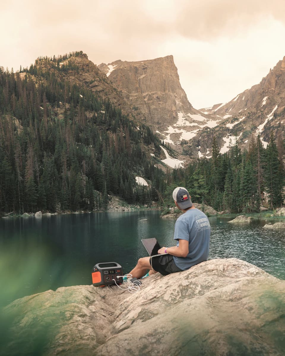 A person working on a laptop by a lake, powered by a portable power station